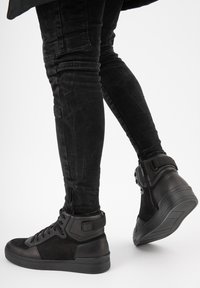 Sneakers neri alto in pelle scamosciata e cuoio, con finitura testurizzata, chiusura con lacci, caviglia imbottita e cinturino regolabile.