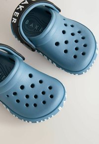 Modré gumové klobúky s perforovaným dizajnom, textúrovaným povrchom a bielym pásikom s logom "BAKER". Má jemný popruh pre bezpečné nosenie.