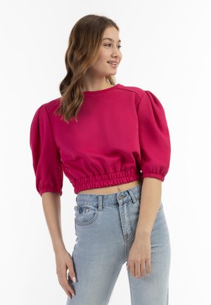 Fuchsiový top se zkrácenými rukávy, balónovými rukávy, elastickým pasem a kulatým výstřihem, kombinovaný se světle modrými džíny s vysokým pasem. Hladká textura látky.