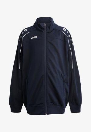 Giacca zip-up blu navy con colletto alto, accenti bianchi e tasche laterali. Presenta il logo "JAKO" e dettagli grigi circolari sulle spalle.