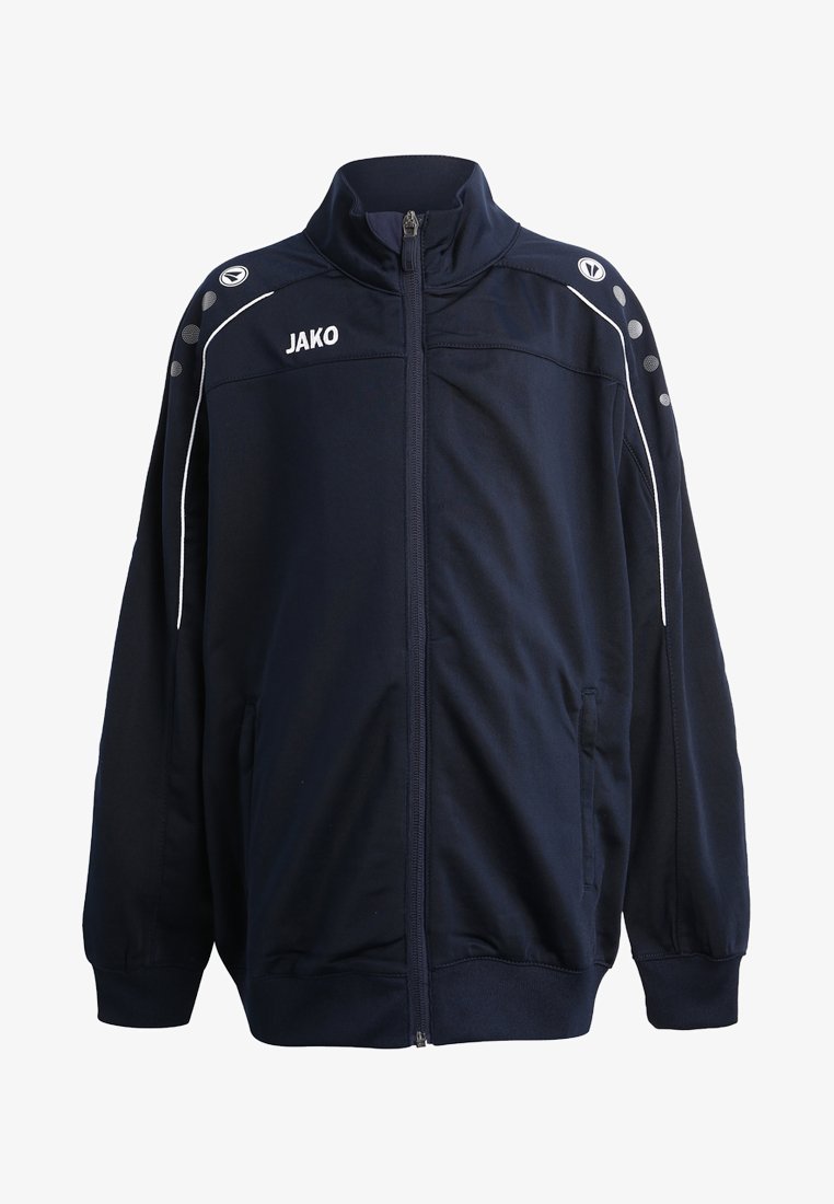 Giacca zip-up blu navy con colletto alto, accenti bianchi e tasche laterali. Presenta il logo "JAKO" e dettagli grigi circolari sulle spalle.
