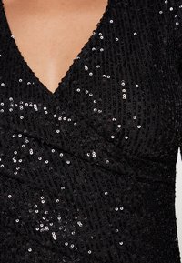 Black dress with a deep V-neck and wrap design. The fabric is textured with numerous sequins reflecting light.