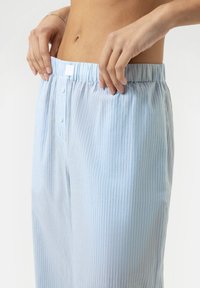 Lichtblauwe gestreepte pyjamabroek met een elastische tailleband en knoopsluiting, met een zachte stoffen textuur en een verticaal streeppatroon.