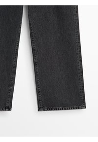 Jambes de jeans en denim noir avec des ourlets coupés droits affichés sur fond blanc.