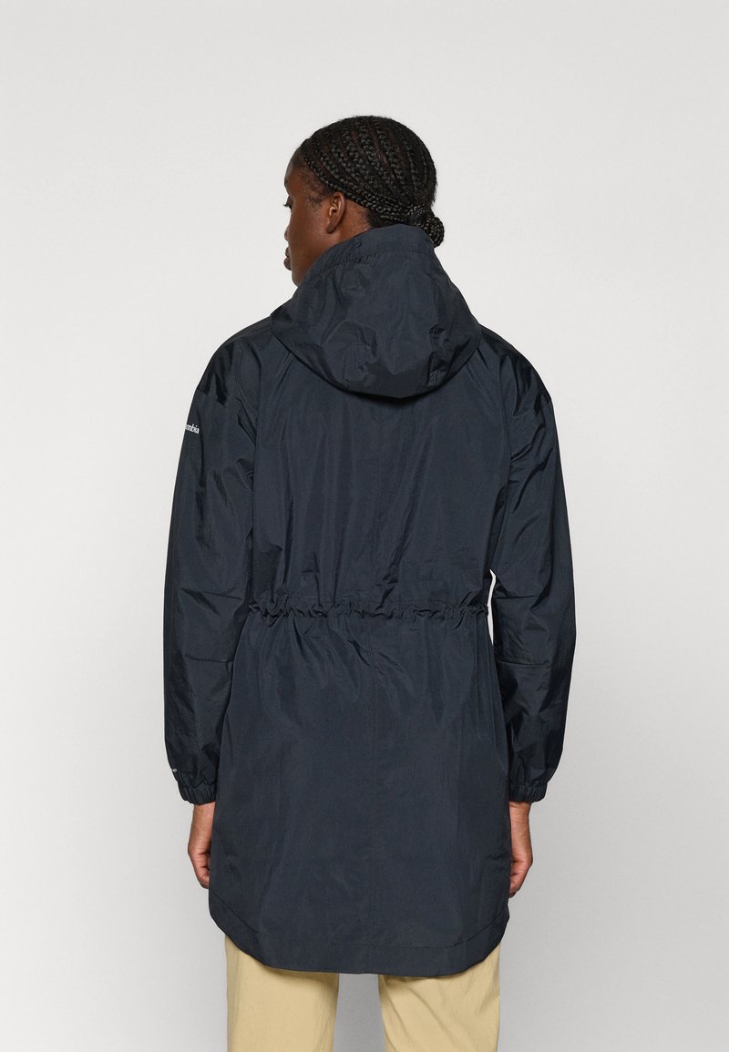 Veste imperméable bleu marine avec capuche, taille élastique et manches longues. Elle présente une texture lisse et un dos légèrement plus long.