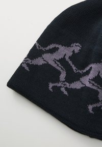 Crna pletenina sa ponovljenim uzorkom ljubičastih stiliziranih ljudskih figura u pozama trčanja.