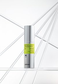 Bouteille cylindrique argentée de sérum raffermissant Celimax Retinol Shot avec étiquette verte, présentée sur une surface en verre transparent devant un fond géométrique blanc.