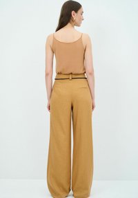 Bruine mouwloze top gecombineerd met hoge, brede beige broek met een gevlochten riem en zakken. Eenvoudig ontwerp en een gladde textuur.