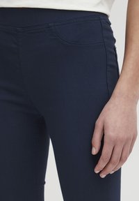Tmavomodré slimky vyrobené z mäkkého, elastického materiálu. Vlastnosti zahŕňajú jemné stehy a dizajn prednej vrecka.