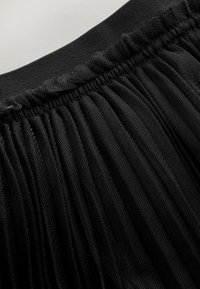 Falda de tul negra con cintura fruncida. Diseño texturizado y fluido con múltiples capas que aportan volumen y movimiento.