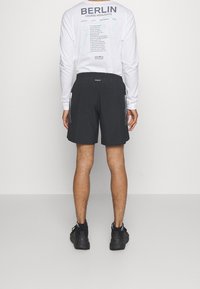 Shorts de sport noirs en matériau léger, dotés de poches latérales et d'une taille à cordon, associés à une chemise blanche à manches longues.