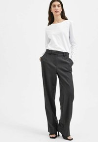 Camicia bianca a maniche lunghe abbinata a pantaloni grigi a vita alta, con una vestibilità sartoriale e design a gamba dritta. Texture del tessuto liscia.