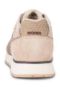 Baskets beiges avec un mélange de matériaux en daim et en maille texturée. Elles présentent une semelle blanche et la marque "WODEN" en brun sur le talon.