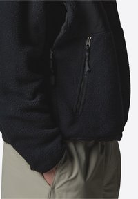 Czarna kurtka polarowa o teksturowanej powierzchni, z dwoma kieszeniami na zamek z przodu i gładką podszewką wewnętrzną.