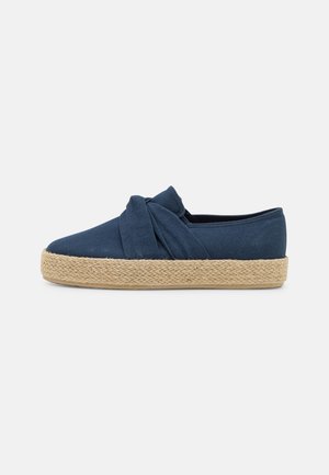Navyblaue Canvas-Slipper mit gedrehtem Stoffdetail, Jute-Seil-Zwischensohle und flacher Gummisohle, die eine glatte Textur aufweist.