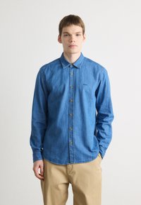 Camicia di jeans blu con bottoni e colletto a punta, bottoni dorati e un piccolo logo sul petto. Maniche lunghe e orlo curvo.