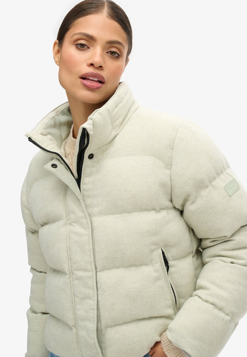 Gevoerde olijfgroene jas met een hoge kraag, ritssluiting, zijzakken en ribgebreide boorden. Kenmerkt zich door een subtiele textuur en een strak ontwerp.