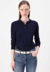 Pullover navy com textura em canelado, colarinho, três botões e cintura ajustada. Combinado com jeans azul claro e um cinto branco.