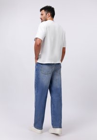 Camiseta blanca de cuello redondo combinada con unos vaqueros de denim de corte holgado en azul claro, con una textura desgastada y dos bolsillos traseros. Zapatillas deportivas blancas.