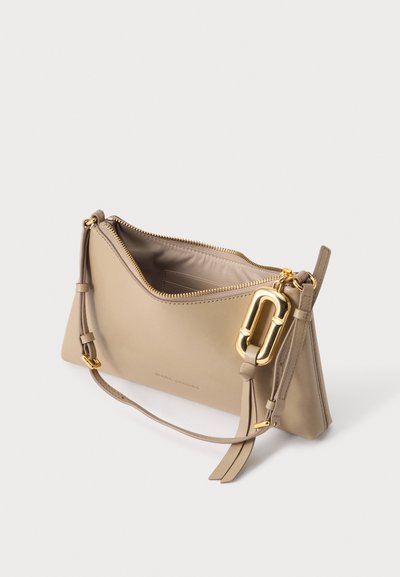 Pochette en cuir beige Marc Jacobs avec fermeture éclair dorée, bracelet ajustable et grande boucle décorative dorée sur fond blanc.