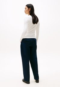 Navy blue, high-waisted trousers with a relaxed fit and two back pockets. Paired with a fitted, long-sleeve white top.