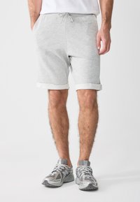Pantalones cortos de algodón gris con cintura con cordón, puños enrollados y bolsillos laterales, combinados con zapatillas deportivas grises que cuentan con detalles de malla.