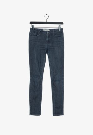 Tmavě modré skinny džíny vyrobené z denimu, s designem pěti kapes, zipovým zapínáním a poutky na opasek. Hladká textura s minimálním vyblednutím.