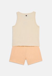 Canottiera beige chiaro con scollo rotondo e logo sul retro, abbinata a pantaloni corti in cotone di colore pesca morbido.