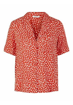 Chemise rouge à manches courtes ornée de points blancs irréguliers, avec un col et une fermeture à boutons, confectionnée dans un tissu léger et texturé.