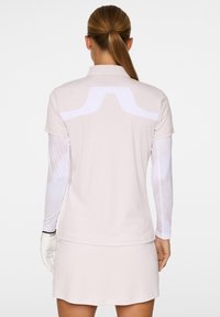 Jasnoróżowa koszulka polo z krótkim rękawem, z białymi akcentami panelowymi na plecach. Długi rękaw biały podkoszulek z wzorem tie-dye.