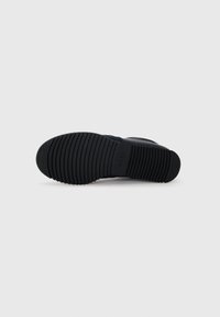 Fekete sneaker talp textúrált barázdákkal; kerek alak; gumi anyag; diszkrét logóval rendelkezik. Minimalista tervezés, tiszta megjelenéssel.