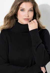 Czarny sweter typu golf z prążkowaną fakturą i długimi rękawami, z wysokim kołnierzem i luźnym fasonem. Gładki materiał, minimalistyczny design.
