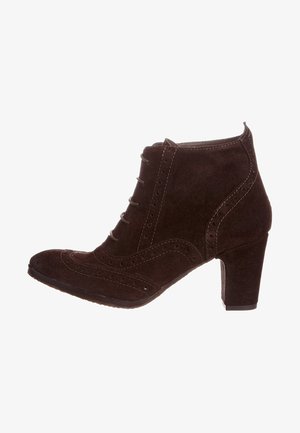 Botte chelsea en daim marron avec un bout arrondi, des détails brogue décoratifs, six œillets et un talon empilé. Texture lisse et design ajusté.