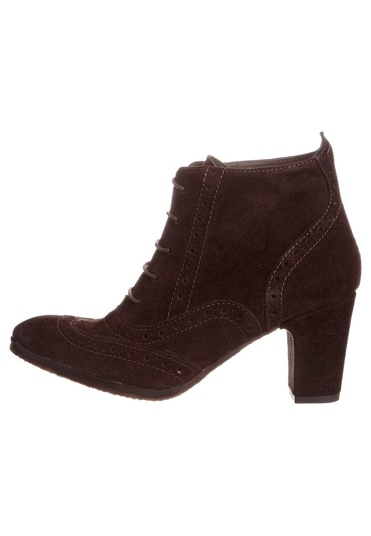 Stivale alla caviglia in suede marrone con punta arrotondata, dettagli brogue decorativi, sei occhielli e tacco impilato. Texture liscia e design aderente.