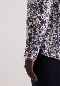 Camicia floreale a maniche lunghe bianca, con un motivo multicolore che presenta tonalità di blu, verde e marrone, completata da polsini con bottoni.