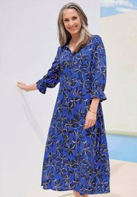 Abito floreale blu con maniche lunghe e arricciate, caratterizzato da un'apertura con bottoni e una silhouette fluente, decorato con motivi di foglie neri e beige.