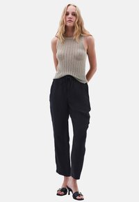 Beige stickad linne med ribbad textur, i kombination med lösa svarta byxor och svarta klackmules med dekorativ detalj.