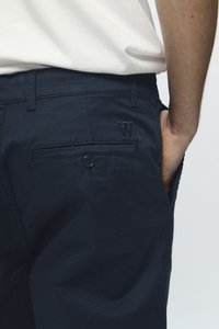 Navy blue cotton shorts with a smooth texture, featuring a back pocket with a button closure and an embroidered logo on the waistband.