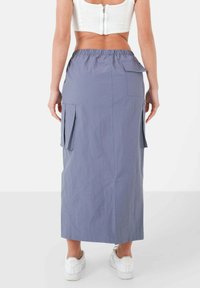 Langer, hellgrauer Rock mit gerafftem Bund, seitlichen Taschen und gerader Silhouette, kombiniert mit weißen Sneakern. Entworfen für lässige Outfits.