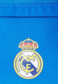 Plava tkanina s teksturiranom površinom ima okrugli logo. Emblem uključuje krunu i bijelu kružnicu s zlatnim i tamnoplavim akcentima.