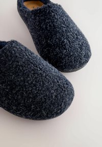 Navy blue indoor slippers with a textured, fuzzy wool surface and rounded toe design. Soft material and slip-on style for easy wear.