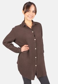 Brown button-up shirt made of textured fabric, featuring a collar, long sleeves, and a relaxed fit with a slightly curved hem.
