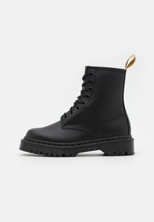 Bottines en cuir noir avec bout arrondi, fermeture à lacets sur le devant, semelle texturée et un onglet de tirage décoratif beige.