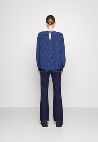 Blusa azul con estampado, de manga larga y detalle de abertura en la espalda, combinada con jeans oscuros de campana y calzado negro. Textura de tela suave.