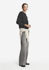 Svart stickad tröja med ribbade ärmar, lager med ett krämfärgat bälte. Ljusgrå utsvängda jeans och blanka svarta skor fulländar outfiten.