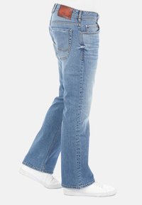 Vaqueros de denim azul claro de pierna recta con bolsillos traseros y laterales, parche de logo de cuero y un discreto desgaste en los muslos.