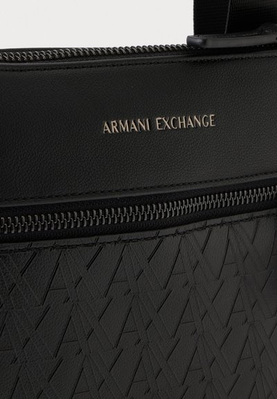Крупен план на черна чанта Armani Exchange със сребристо лого, ципове и релефен геометричен мотив.