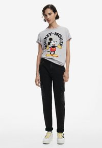 T-shirt gris clair avec un grand graphisme de Mickey Mouse, associé à un pantalon cargo noir et des baskets à plateforme blanches avec des lacets jaunes.