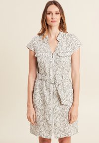 Vestito leggero a maniche corte beige con motivo fogliare, chiusura con zip frontale, due tasche e vita con cintura. Vestibilità casual.