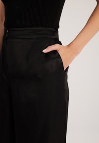 Zwarte broek met een soepele textuur en een wijdbeenontwerp, voorzien van een zijzak en een aansluitende tailleband.